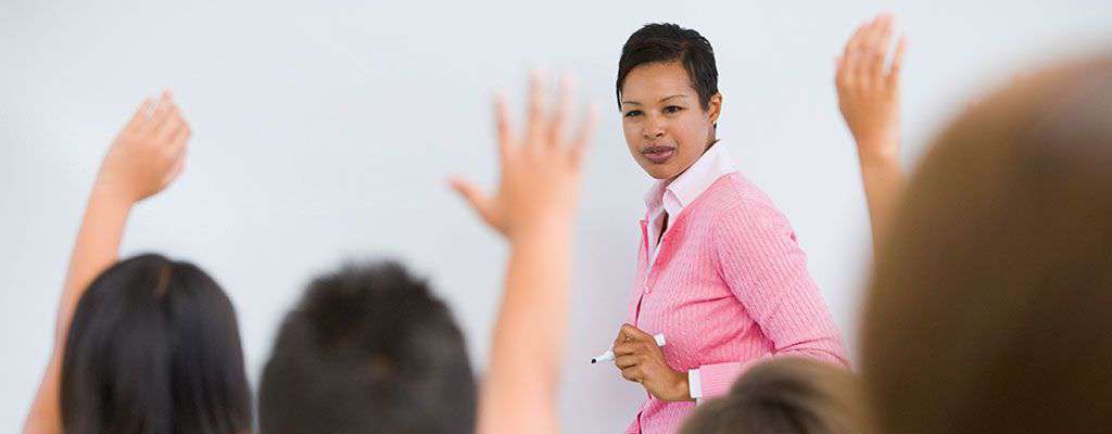 teacher at white board while students raise their hand